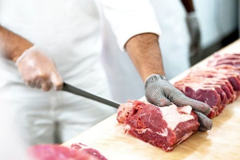 Personne équipée découpant plusieurs morceaux de viande fraîche sur une planche en bois dans un environnement professionnel