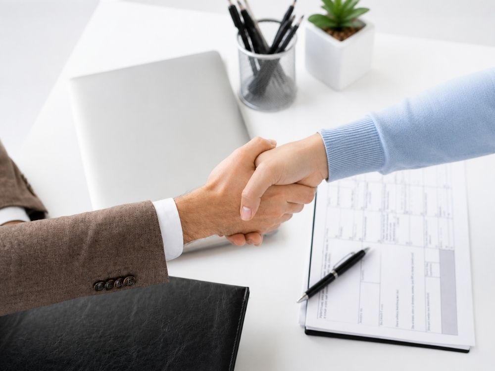 Deux personnes se serrant la main au-dessus d’un bureau, symbolisant un engagement professionnel et des garanties de confiance