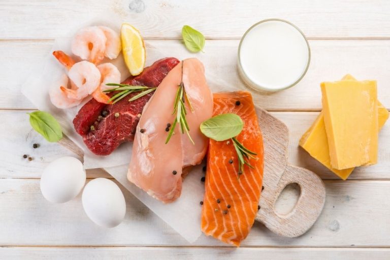 Assortiment de produits alimentaires avec crevettes, viande de bœuf, filet de poulet, pavé de saumon, fromage, œufs durs et verre de lait sur une planche